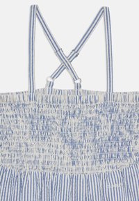 Dryžuota suknelė su surinktu liemeniu, su mėlynos ir baltos vertikalios juostos, reguliuojamos petnešos kryžminės už nugaros ir minkšta audinio tekstūra.