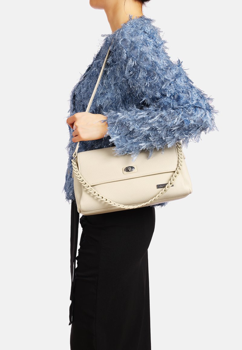 Borsa a spalla in pelle beige con tracolla intrecciata, caratterizzata da una chiusura magnetica centrale e una finitura testurizzata, portata insieme a una giacca blu testurizzata.