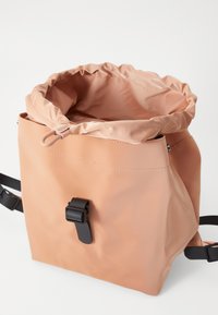 Péachfarga roll-top veske laget av glatt, vanntett materiale. Har en svart lås og justerbare stropper for sikker lukking.