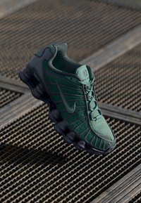 Zapatilla Nike en verde y gris, con un upper texturizado, malla ligera y una suela única acolchada con unidades de amortiguación redondeadas.