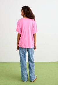 T-shirt rose oversize à manches courtes, vue arrière. Associé à un jean large bleu clair et des chaussures à plateforme beige. Design simple, sans motifs visibles.