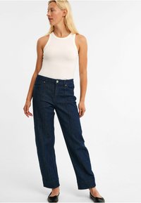 Dunkelblaue Jeanshose mit geradem Bein, kombiniert mit einem weißen gerippten Tanktop. Verfügt über sichtbare Nähte und Vordertaschen.