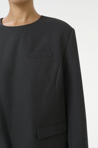 Svart strukturert blazer med rund hals, subtile lomme detaljer og et teksturert stoff med en jevn finish.