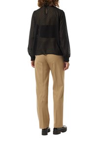 Schwarze durchsichtige Bluse mit Polka-Dots, langen Puffärmeln und einem Schlüsselloch-Rücken, kombiniert mit beigefarbenen, taillierten Hosen und schwarzen Schuhen.