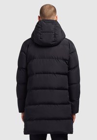 Fekete puffermellény, kapucnival, steppelt dizájnnal, hosszú ujjakkal és térd középig érő hosszal. Sima textúra, látható díszítések nélkül.