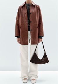 Brown leather coat with button closure, beige trousers, and a dark brown suede bag. White shoes complete the outfit.