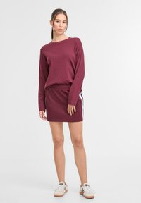 Felpa bordeaux con maniche lunghe abbinata a una gonna coordinata con righe laterali. Tessuto morbido, vestibilità rilassata e vita elasticizzata.
