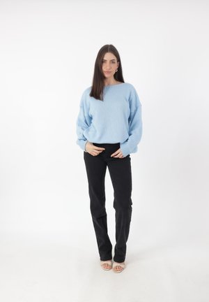 Lichtblauwe gebreide trui met brede mouwen, gecombineerd met zwarte strakke broeken en beige sandalen. Eenvoudige, casual outfit met een relaxte pasvorm.