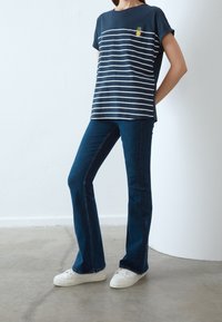 Marine gestreepte t-shirt met korte mouwen en een ananas borduursel op de borst, gecombineerd met donkerblauwe flare jeans en witte sneakers.
