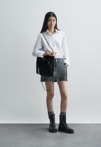 Black leather skirt with front zipper, white button-up shirt, black fringe crossbody bag, and black combat boots with gold accents.