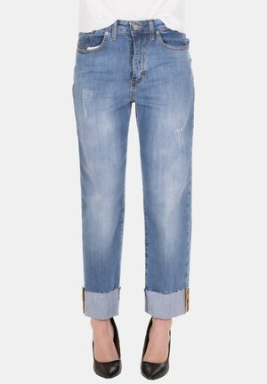 Jeans blu chiaro a vita media con orli risvoltati, leggero effetto consumato, indossati con décolleté nere a punta e top bianco visibile in vita.