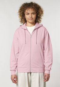 Felpa rosa con cappuccio zip, realizzata in materiale morbido, con una cerniera frontale, coulisse e due tasche anteriori. Vestibilità oversize con polsini a coste.