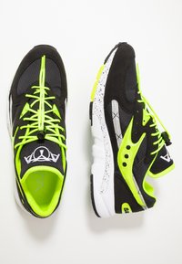 Scarpe da ginnastica in bianco e nero con accenti verde neon, tessuto testurizzato, pannelli in rete e suole maculate. Presentano lacci elastici e dettagli con logo.