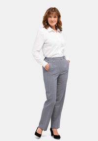 Witte overhemd met lange mouwen, gecombineerd met grijze op maat gemaakte broek met zijzakken en een subtiel ruitpatroon. Zwarte hakken.