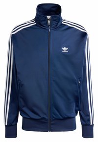 Giacca sportiva Adidas blu navy con tre strisce bianche sulle maniche, zip frontale, tasche con zip e logo Adidas sul petto.