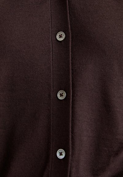Detailní záběr na tmavě hnědou pletenou látku se třemi vertikálně seřazenými kulatými knoflíky, z nichž každý má čtyři dírky přišité tmavým nitěm.