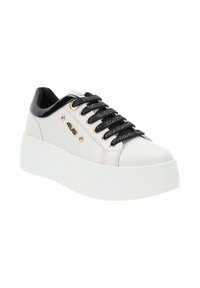 Zapatilla de cuero blanca con una textura suave, acentos de charol negro, ojales metálicos y cordones a rayas en negro y plata. Suela blanca gruesa.