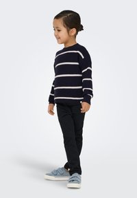 Pull rayé marine à lignes blanches, pantalon foncé et chaussures à enfiler bleues. Le pull a un col arrondi et des poignets côtelés.