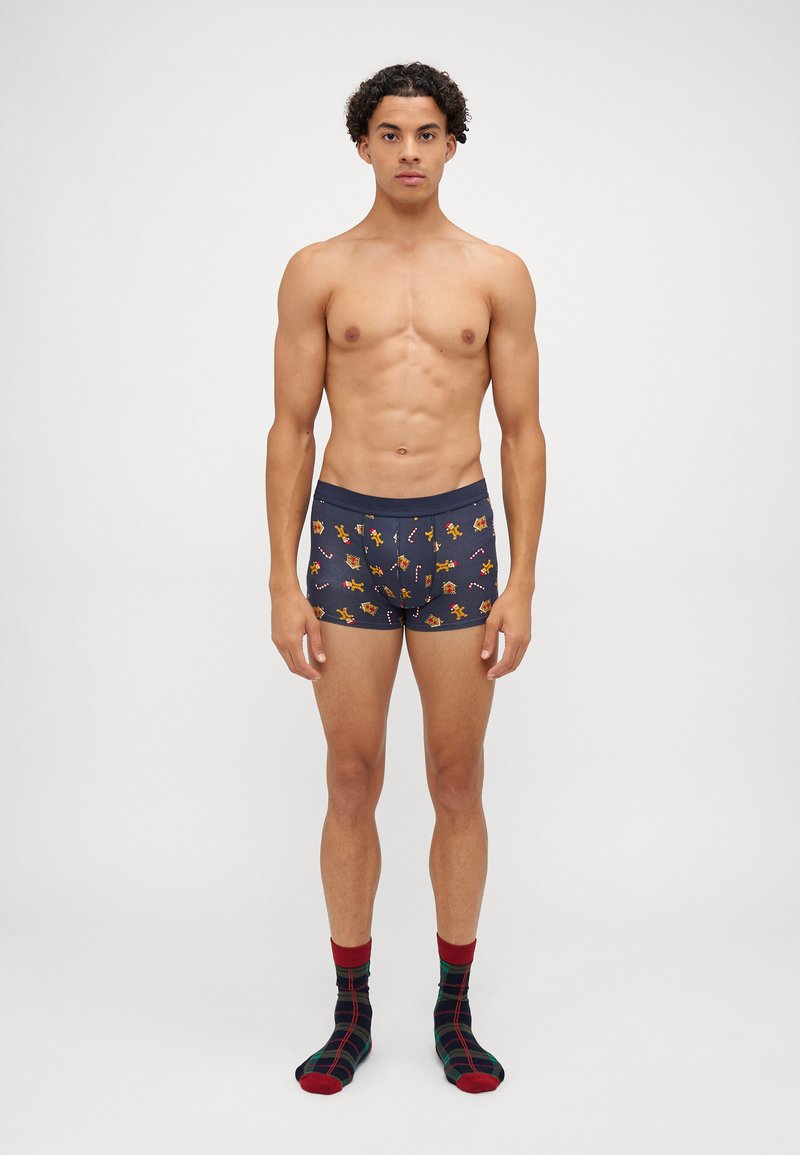 Marinblå boxershorts med färgglada mönster av blommor och geometriska former, i kombination med svart och röd rutiga strumpor.