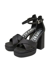 Sandalias de plataforma negras de tacón alto con diseño de tiras cruzadas, parte superior texturizada, tacón ancho y correa ajustable en el tobillo. Etiqueta de la marca visible en el interior.