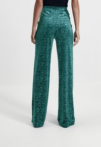Zielone spodnie o szerokich nogawkach w panterkę z wysokim stanem i gładką fakturą, z tylnymi kieszeniami i miękkim, aksamitnym wykończeniem.