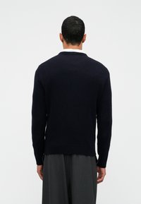 Mornarsko plava pletena majica sa okruglim izrezom i rebrastim detaljima, s teksturiranom završnicom i opuštenim krojem, prikazana sa stražnje strane.