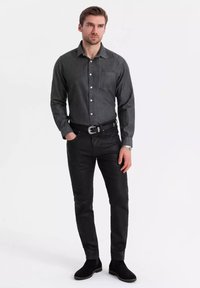 Chemise gris à boutons avec une poche poitrine, associée à un pantalon noir ajusté et des bottines. Tissu lisse, coupe cintrée, détails minimalistes.