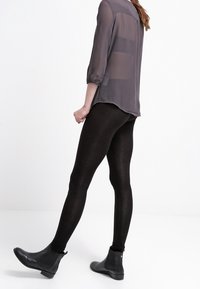 Transparent, långärmad grå blus med insydda manschetter, parat med svarta leggings och ankelstövlar. Blusen har horisontella randmönster.