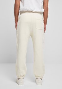 Pantaloni de trening de culoare crem, confecționați dintr-un material moale, având un brâu cu șnur, mansete elastice și un singur buzunar pe spate.