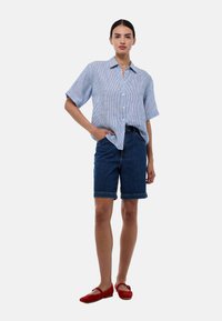 Chemise à rayures bleu clair à manches courtes, associée à un short en denim bleu foncé et des chaussures plates rouges. Coupe structurée, décontractée.