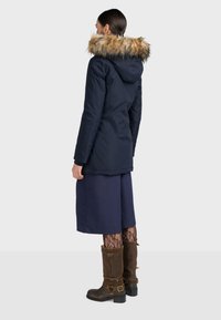 Námornícky modrá parka s umelou kožušinou na kapucni, s úzkym strihom a dlhými rukávmi. V kombinácii s námorníckou sukňou, vzorovanými pančuchami a hnedými čižmami.