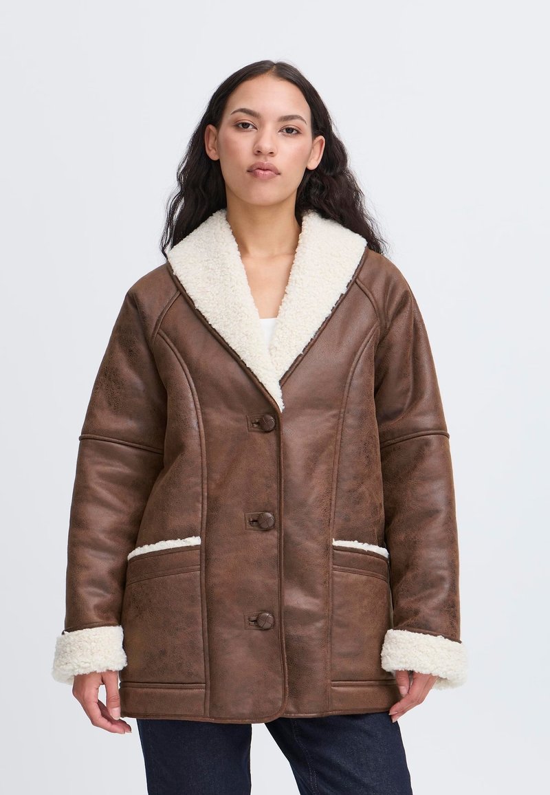 Giacca in pelle marrone con un morbido colletto e polsini in shearling bianco. Presenta una chiusura a bottoni e tasche frontali con dettagli bianchi.