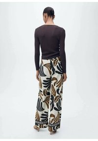 Haut à manches longues côtelé marron associé à un pantalon large arborant un motif floral noir, marron et crème. Rehaussé d'une bordure décorative.