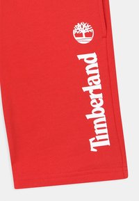 Punaiset puuvillashortsit, joissa on suuri valkoinen "Timberland"-teksti ja logo sivussa. Kangas on sileäpintainen ja kevyt.