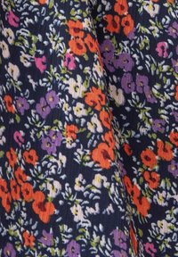 Tissu bleu foncé avec un motif floral dense en fleurs orange, violettes, blanches et feuilles vertes, montrant une texture et de légères plissures.