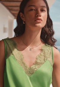 Green satin top with lace trim at the neckline, featuring a V-cut design. Model wears a delicate gold necklace with a round charm.