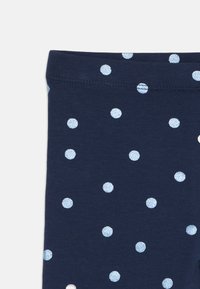 Primo piano di un tessuto blu navy con pois glitterati blu chiaro e cuciture della vita ben visibili.