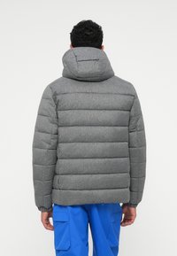 Grå vadderad jacka med huva, med en quiltad design och ribbade ärmslut. Baksidan visar sömdetaljer och strukturerad tyg.