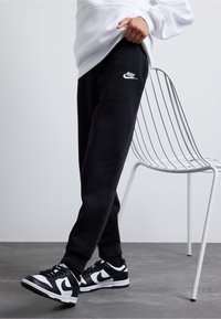 Colanți Nike negri cu logo alb, având un design conic și manșete elastice. Asortați cu adidași Nike negri și albi.