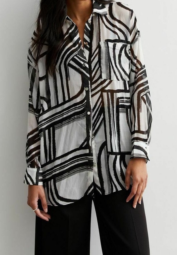 Femme portant une chemise à manches longues boutonnée avec des lignes géométriques abstraites en noir et blanc et un pantalon noir.