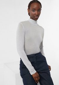 Grauer langärmeliger Rollkragenpullover aus weichem, leichtem Material, kombiniert mit dunklen Hosen, die ein enganliegendes Design und nahtlose Bündchen aufweisen.