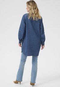 Denim srajca, dolgi rokavi, sproščen kroj, modra barva, stranske odprtine, zapnjen manšeti, v kombinaciji s svetlo modrimi širokimi jeans hlačami, obuta v taupe pete.