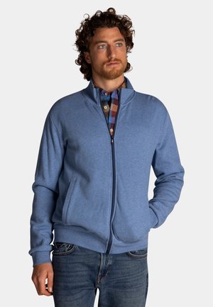 Lichtblauwe ritsvest met een staande kraag, voorzien van lange mouwen en voorzakken, gedragen over een geruit shirt.