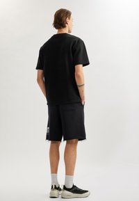 Camiseta negra de gran tamaño con mangas cortas, combinada con pantalones cortos negros deshilachados. Zapatillas negras y blancas con calcetines gris claro.