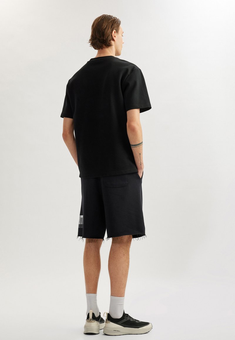 Sort oversized t-shirt med korte ærmer, parret med sorte slidte shorts. Sorte og hvide sneakers med lysegrå sokker.