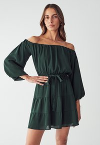 Grünes schulterfreies Kleid aus leichtem Material. Es hat Puffärmel, eine taillierte Taille mit einem Bindeband und einen gestuften Saum.