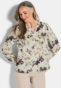 Blusa a maniche lunghe in tessuto leggero, con una base crema decorata da motivi floreali marroni e grigi, un collo henley e dettagli di bottoni sottili.