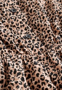 Béžová látka s černým leopardím vzorem, s dvěma černými knoflíky a shrnutými elastickými detaily.