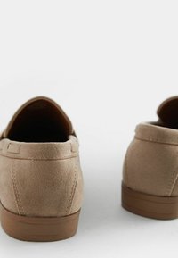 Chaussures en daim beige avec un bout rond, semelle plate marron et détails cousus autour du col. Surface texturée avec une finition lisse.