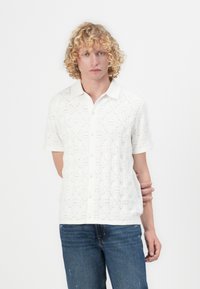 Witte overhemd met korte mouwen, met een gestructureerd ruitpatroon en kleine oogjes, gecombineerd met blauwe denim jeans.